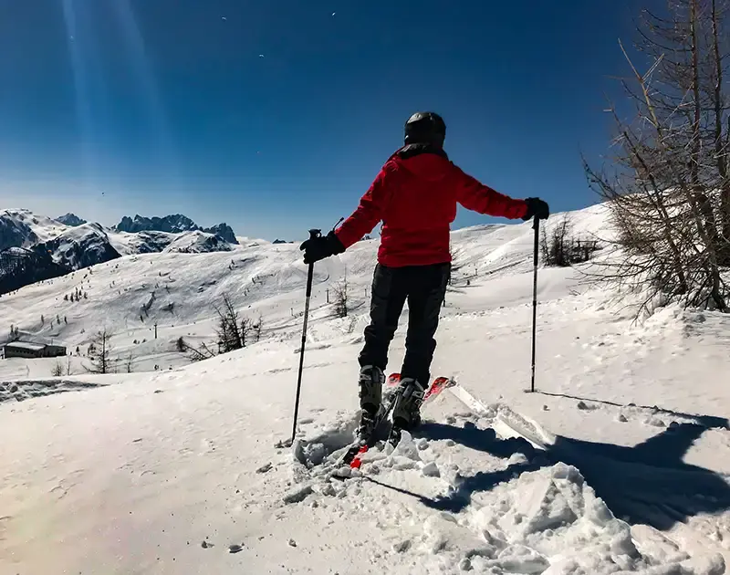 Schifahrer in rotem Anorak und Schihelm steht am Rand der Schipiste und schaut ins Tal