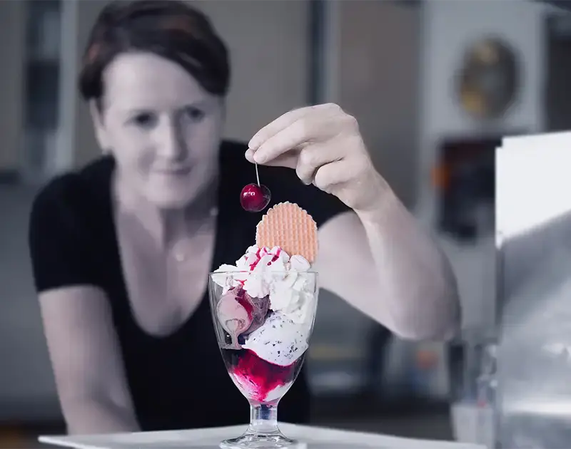 Eine Frau dekoriert einen Eisbecher mit einer Kirsche