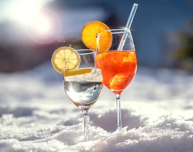 Two glasses of white wine and Aperol Spritz stand in the snow 